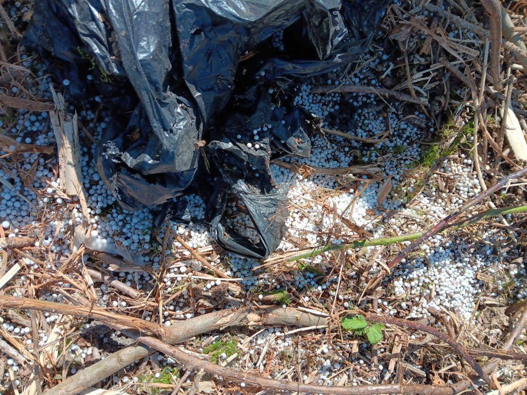Black plastic bag on the ground, surroounded by thousands of tiny polystyrene beads.