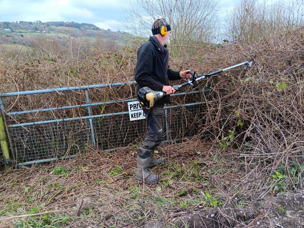 Simon wearing ear defenders and holding a large petrol strimmer, attacking the brambles.